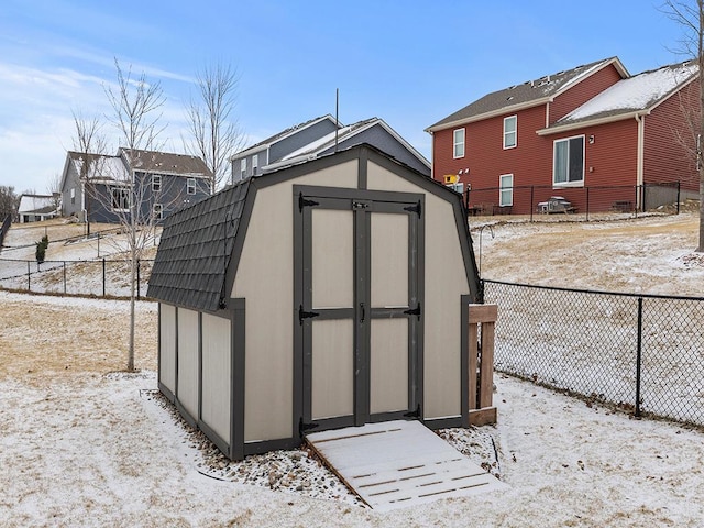 snow covered structure featuring an outbuilding, a storage unit, and fence