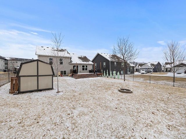 rear view of property featuring an outdoor fire pit, a residential view, a storage unit, fence, and a wooden deck