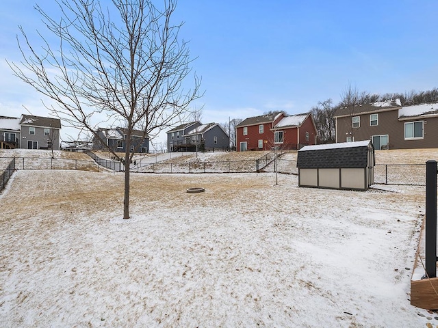 snowy yard featuring a storage shed, an outdoor structure, fence, and a residential view