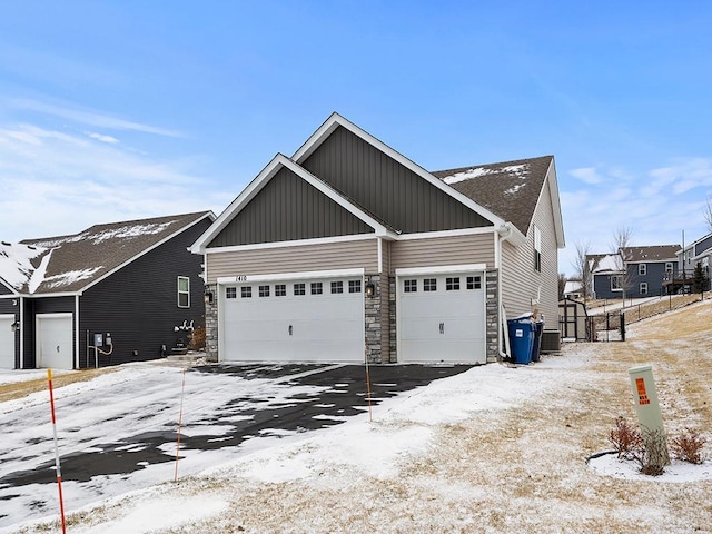 view of snowy property featuring a garage, stone siding, central AC unit, and board and batten siding