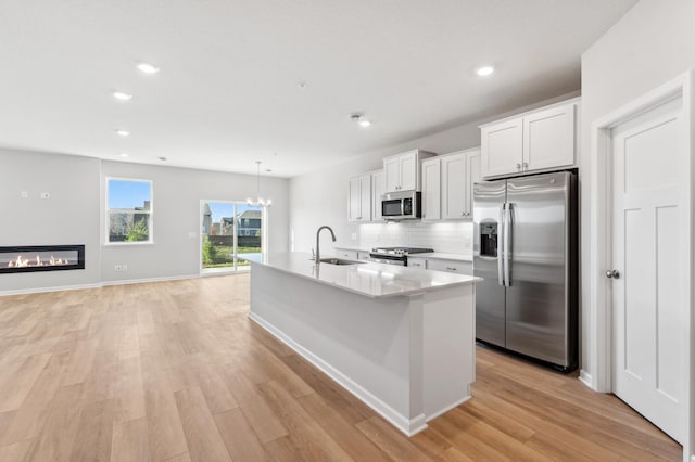 kitchen featuring appliances with stainless steel finishes, an island with sink, sink, white cabinets, and light wood-type flooring