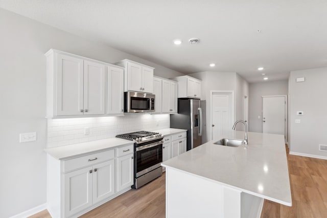 kitchen with sink, tasteful backsplash, an island with sink, stainless steel appliances, and white cabinets