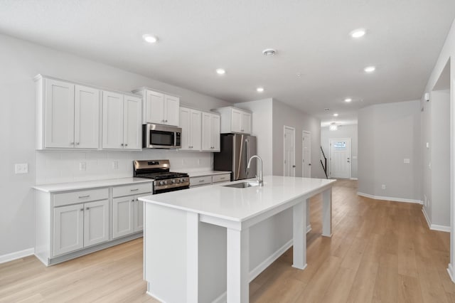 kitchen featuring tasteful backsplash, a kitchen island with sink, stainless steel appliances, light wood-style floors, and a sink