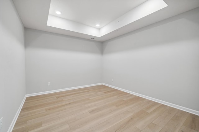 unfurnished room with light wood-type flooring, baseboards, a raised ceiling, and recessed lighting