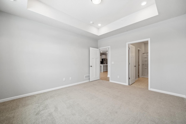 unfurnished bedroom with a tray ceiling, recessed lighting, light colored carpet, visible vents, and baseboards