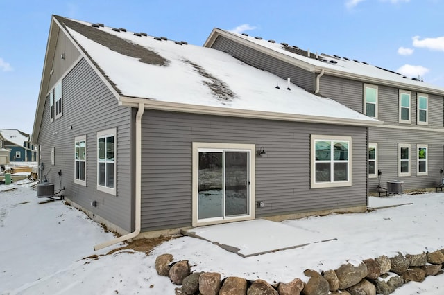 snow covered rear of property featuring central AC unit