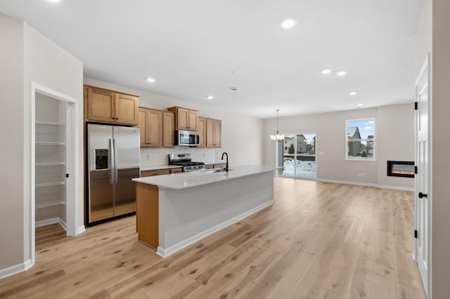 kitchen featuring pendant lighting, sink, a kitchen island with sink, light hardwood / wood-style floors, and stainless steel appliances