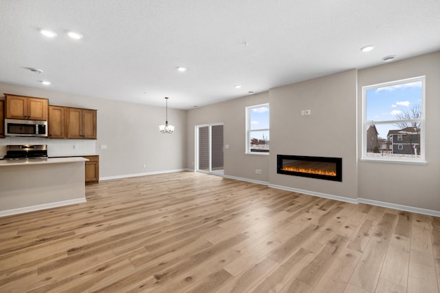 unfurnished living room featuring an inviting chandelier, plenty of natural light, and light hardwood / wood-style floors