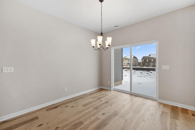 spare room with light wood-style flooring, baseboards, and an inviting chandelier