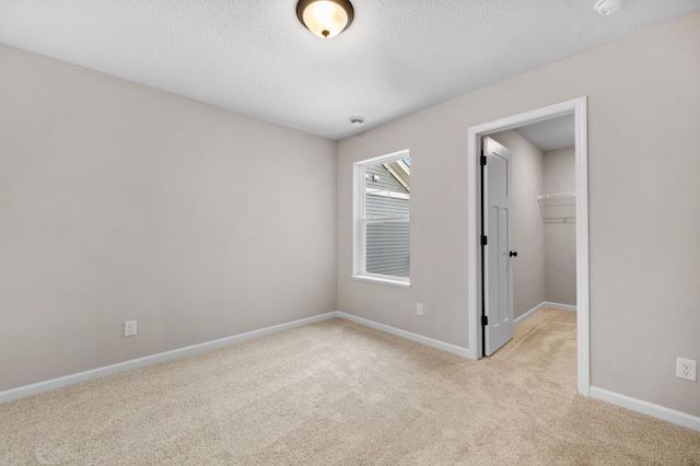 unfurnished bedroom featuring a walk in closet, a closet, light carpet, a textured ceiling, and baseboards