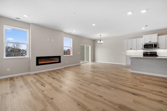 unfurnished living room featuring light wood finished floors, plenty of natural light, and a glass covered fireplace