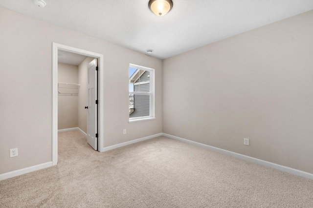 unfurnished bedroom featuring a walk in closet, a closet, carpet flooring, and baseboards