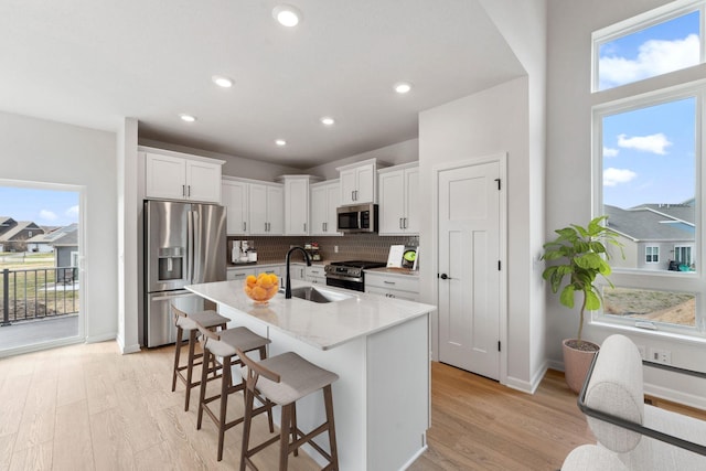 kitchen with light wood-style flooring, a breakfast bar area, stainless steel appliances, white cabinets, and a sink