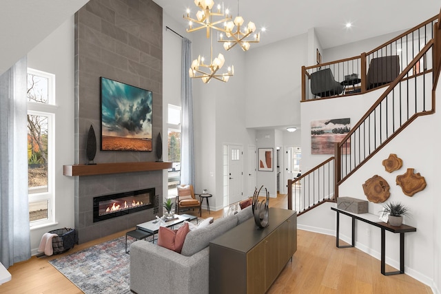 living room featuring baseboards, a tile fireplace, light wood-style flooring, an inviting chandelier, and stairs