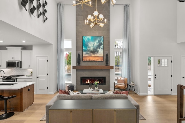 living room with a tiled fireplace, light wood finished floors, a high ceiling, and an inviting chandelier