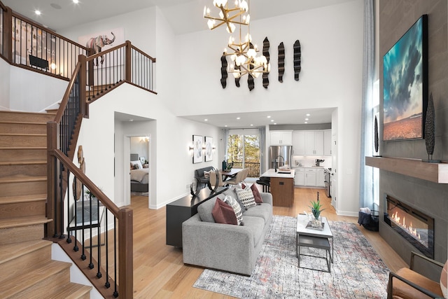 living room featuring light wood-type flooring, a glass covered fireplace, stairway, and an inviting chandelier