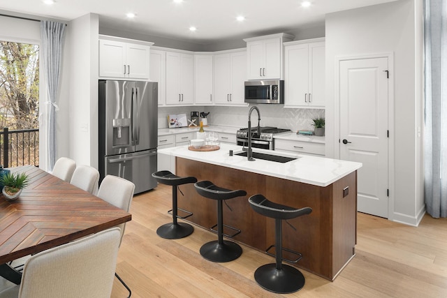 kitchen featuring light wood-style flooring, stainless steel appliances, a sink, backsplash, and an island with sink