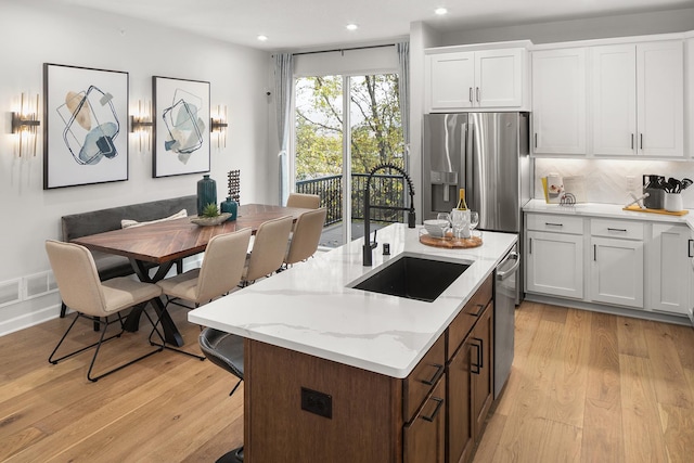 kitchen with light wood finished floors, tasteful backsplash, appliances with stainless steel finishes, white cabinetry, and a sink