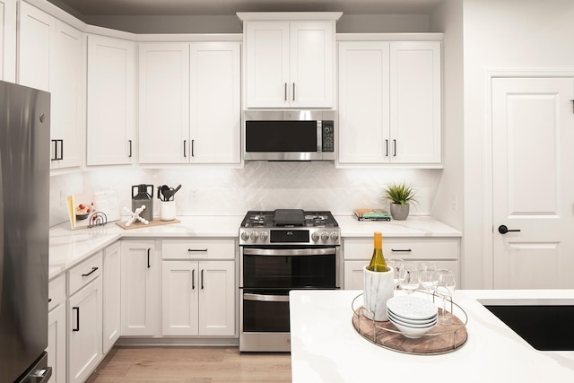 kitchen with white cabinetry, appliances with stainless steel finishes, light stone countertops, light wood finished floors, and tasteful backsplash