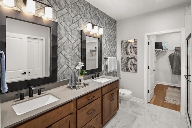 bathroom featuring toilet, marble finish floor, double vanity, and a sink