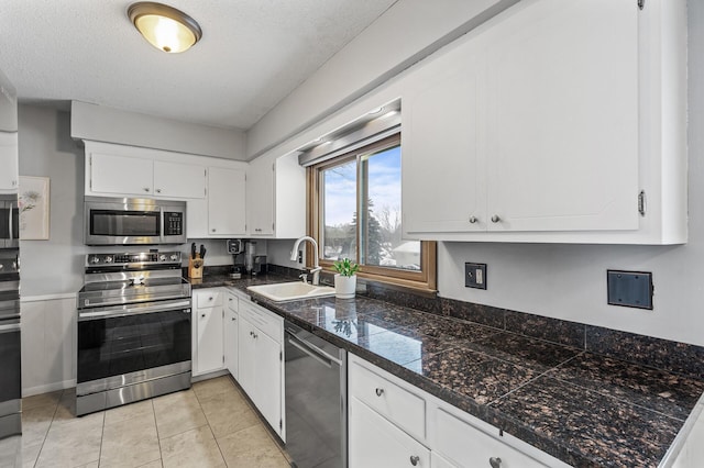 kitchen with appliances with stainless steel finishes, white cabinetry, sink, light tile patterned floors, and a textured ceiling