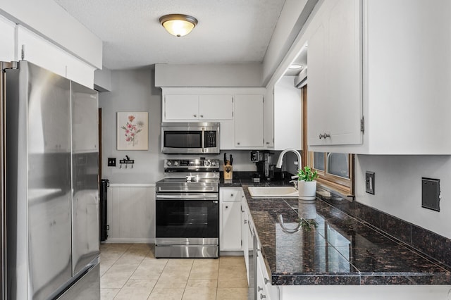 kitchen featuring appliances with stainless steel finishes, white cabinetry, sink, light tile patterned floors, and a textured ceiling