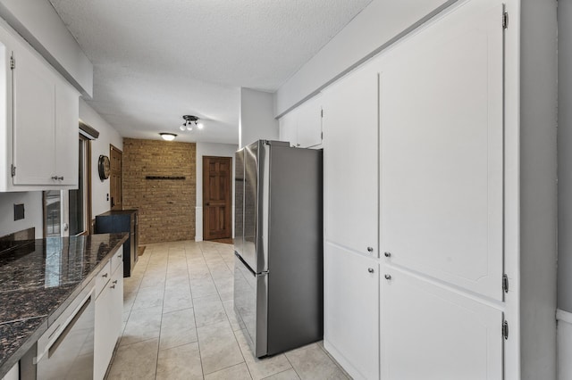 kitchen featuring appliances with stainless steel finishes, white cabinetry, a textured ceiling, brick wall, and light tile patterned flooring