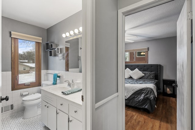 bathroom with tile patterned flooring, tile walls, vanity, a textured ceiling, and toilet