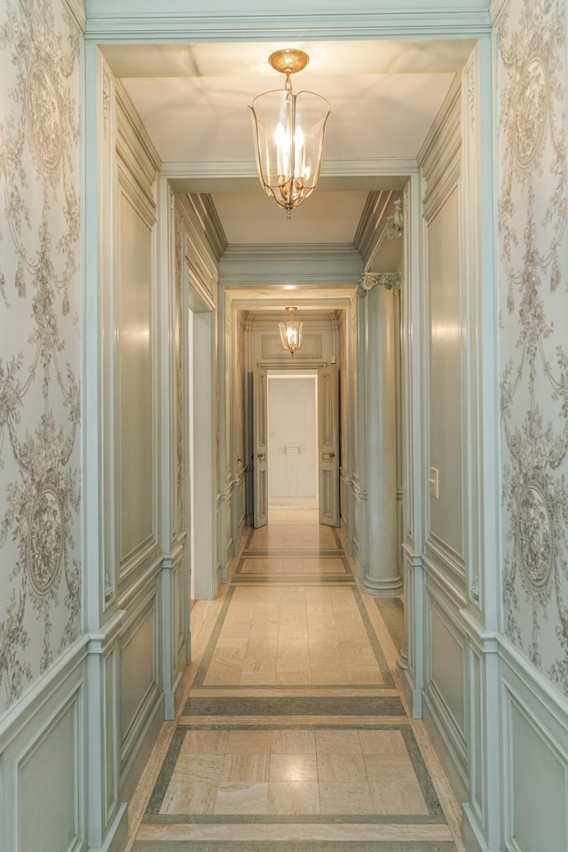 hall with wallpapered walls, wainscoting, a decorative wall, and an inviting chandelier