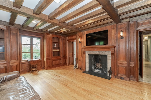 living area with light wood-type flooring, a fireplace with flush hearth, wooden walls, and beam ceiling