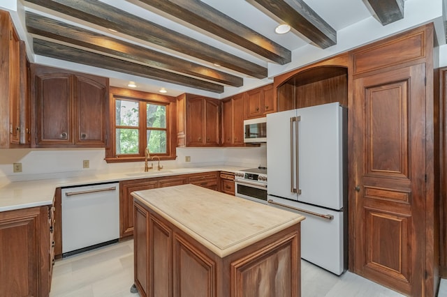 kitchen with white appliances, a kitchen island, brown cabinets, a sink, and beam ceiling