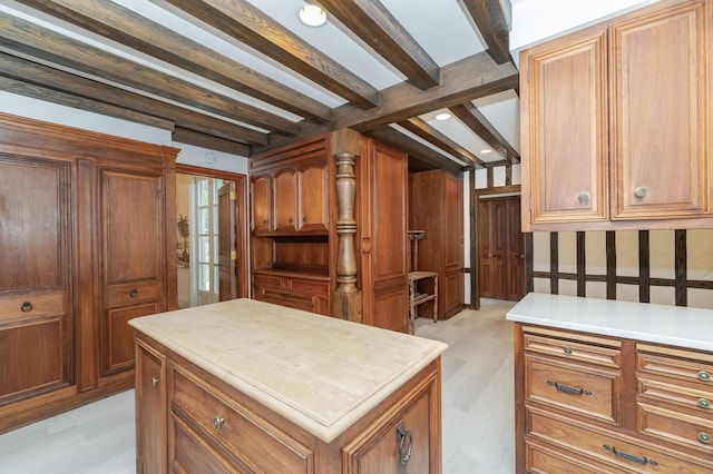 kitchen featuring brown cabinetry, a center island, light countertops, light wood-type flooring, and beam ceiling