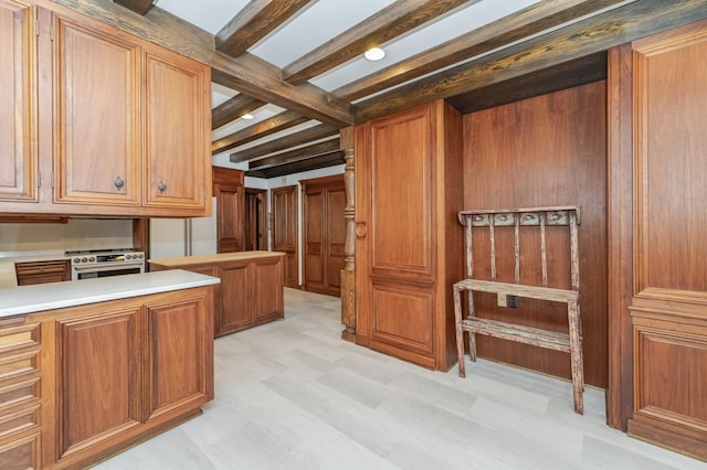 kitchen with brown cabinets, light countertops, stainless steel stove, light floors, and beam ceiling