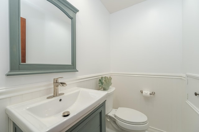 half bathroom with a wainscoted wall, vanity, and toilet