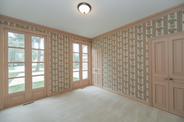 carpeted spare room featuring wallpapered walls, baseboards, visible vents, and ornamental molding