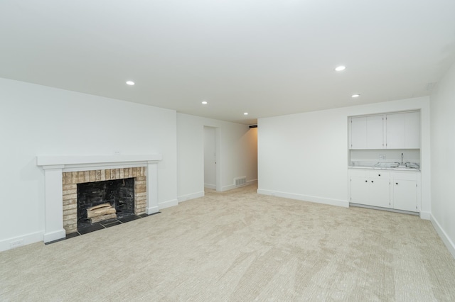 unfurnished living room with a brick fireplace, recessed lighting, a sink, and light colored carpet