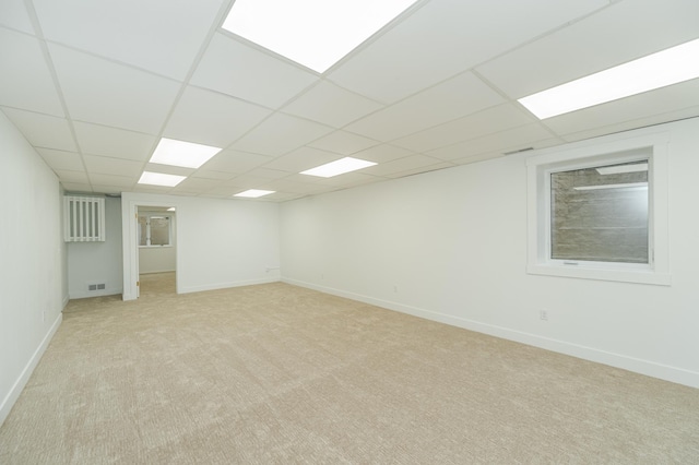 finished below grade area with light carpet, baseboards, visible vents, and a paneled ceiling