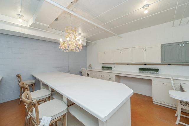 kitchen featuring a breakfast bar, concrete block wall, decorative light fixtures, light countertops, and finished concrete floors