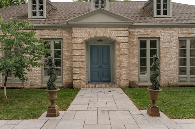 entrance to property with brick siding, roof with shingles, and a lawn