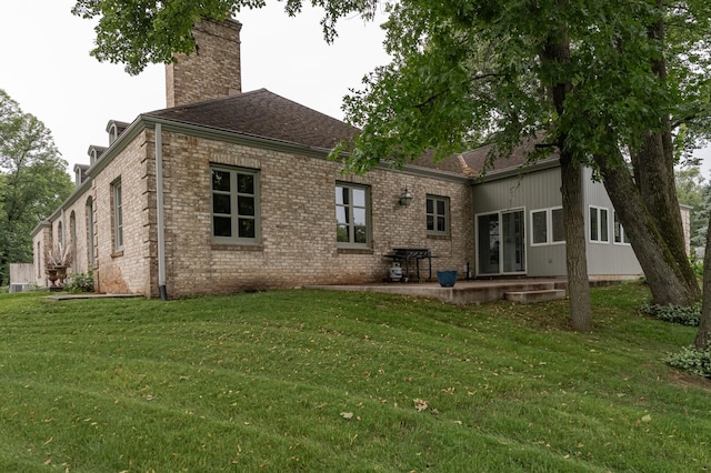 back of house with roof with shingles, brick siding, a patio, a chimney, and a lawn