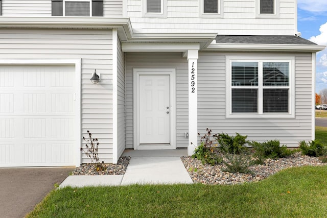 doorway to property with a garage and a lawn