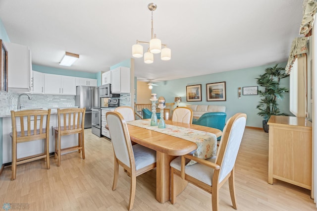 dining space with sink, ceiling fan with notable chandelier, and light hardwood / wood-style floors