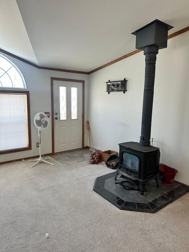 entryway featuring a wood stove, carpet flooring, a wealth of natural light, and ornamental molding