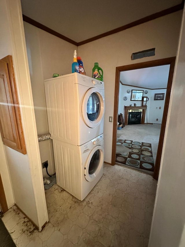 laundry room with laundry area, light floors, stacked washer and clothes dryer, and crown molding