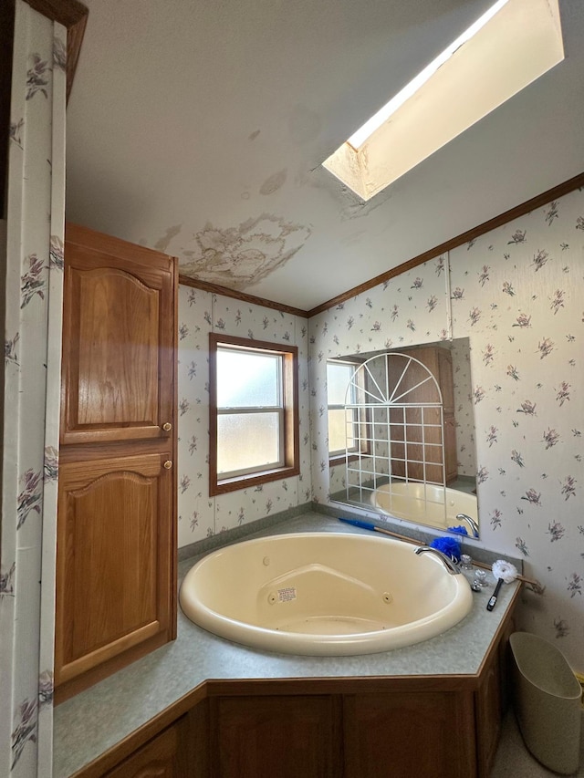 bathroom with vaulted ceiling with skylight, a jetted tub, wallpapered walls, and crown molding