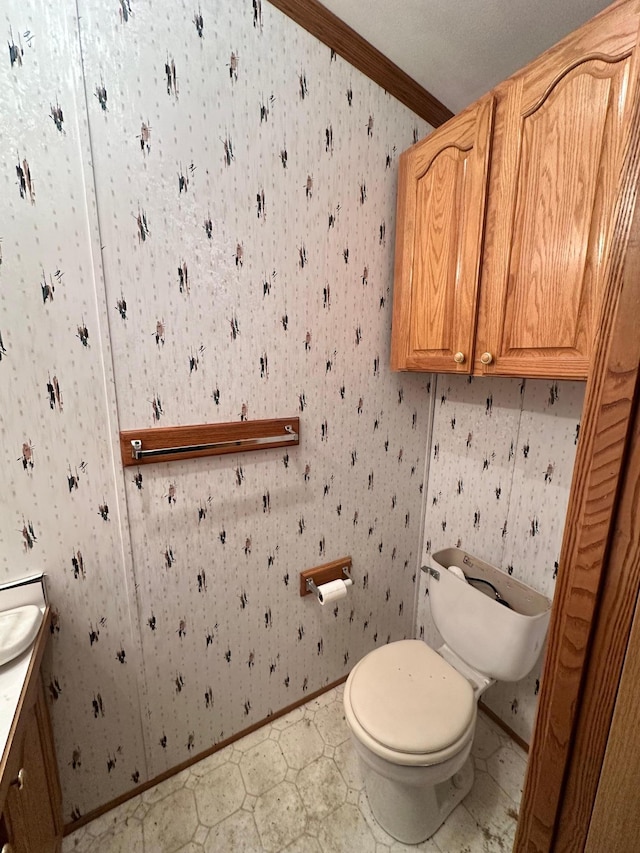 bathroom with vanity, toilet, wallpapered walls, and ornamental molding