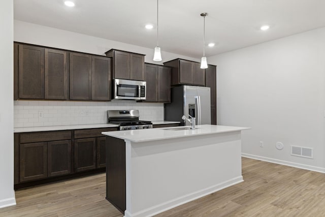 kitchen with sink, dark brown cabinets, hanging light fixtures, a center island with sink, and appliances with stainless steel finishes