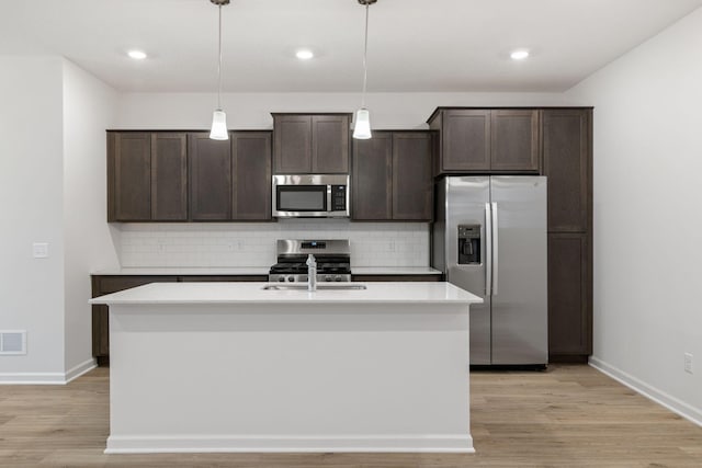 kitchen featuring pendant lighting, dark brown cabinets, stainless steel appliances, and an island with sink