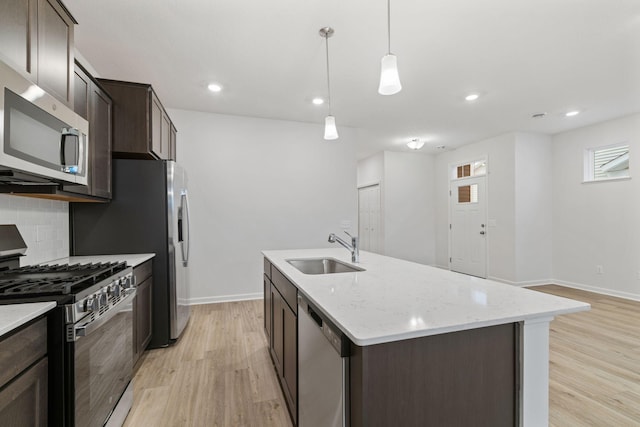 kitchen featuring pendant lighting, sink, stainless steel appliances, light stone countertops, and a center island with sink