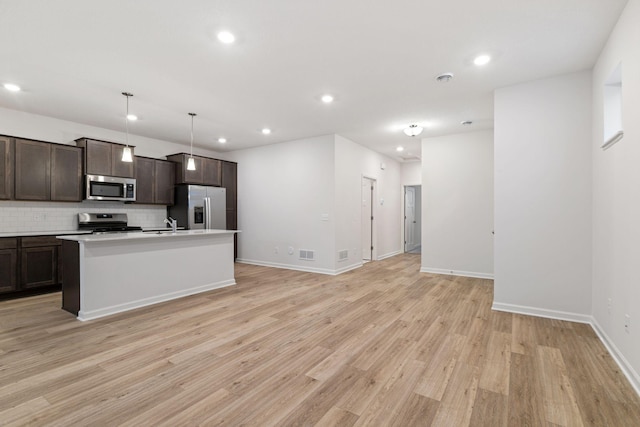 kitchen featuring pendant lighting, light hardwood / wood-style flooring, appliances with stainless steel finishes, a kitchen island with sink, and dark brown cabinets